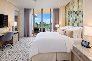 Habitación de hotel con cama, escritorio, silla, televisión y vista a palmeras.