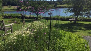 Un jardín tranquilo junto al lago con un banco de madera, un indicador y abundante vegetación.