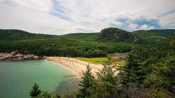 Paisaje costero con una playa, colinas boscosas y cielo despejado.