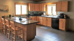Una cocina con armarios de madera, una isla central con taburetes, lavavajillas y un ventanal que proporciona luz natural.