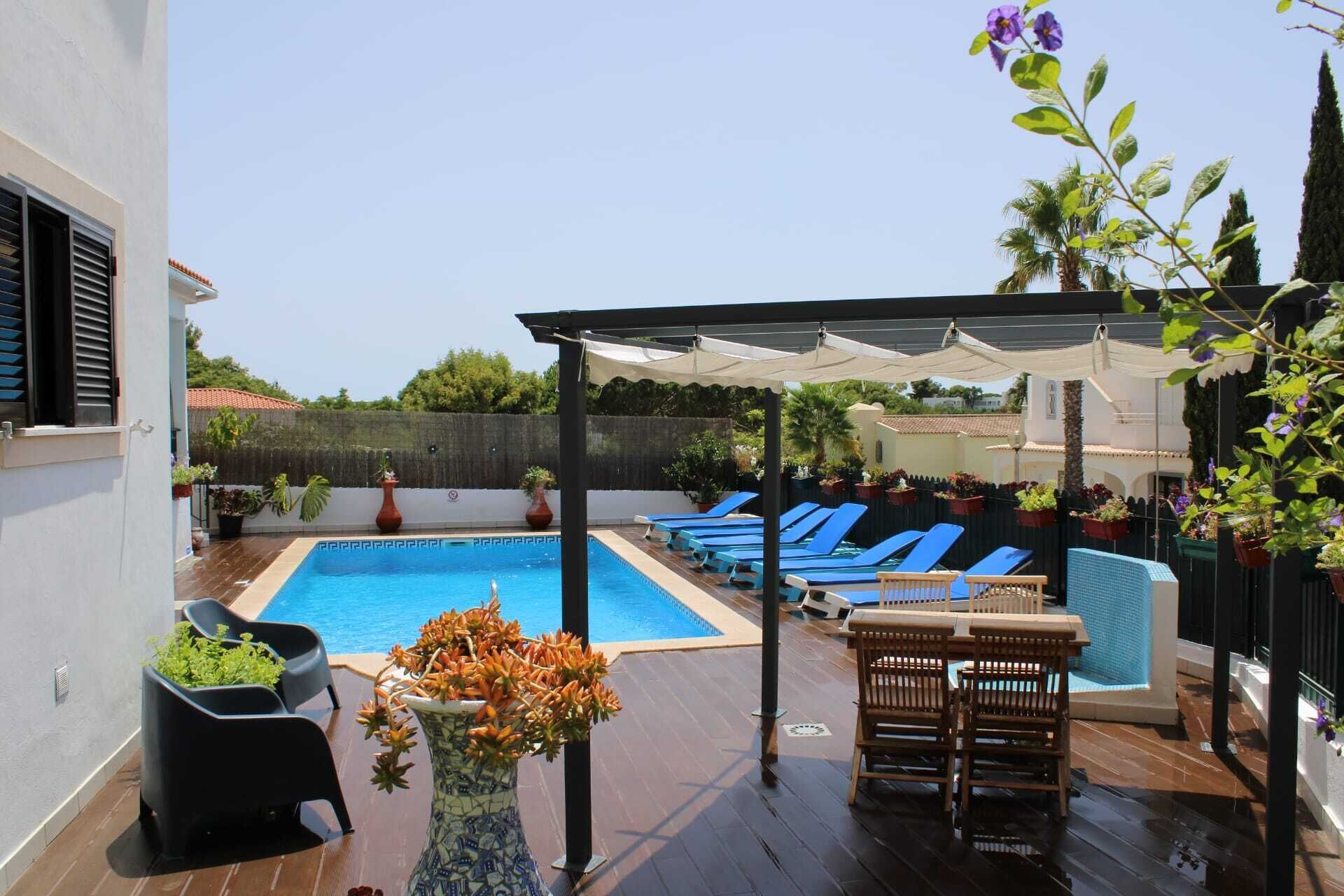 A pool area with blue lounge chairs, a covered seating area, and potted plants.