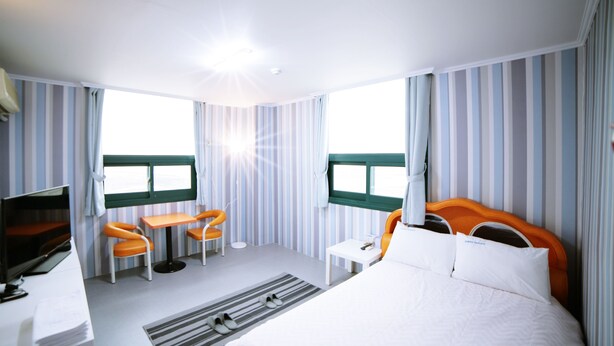 Habitación de hotel con cama, televisor, escritorio, dos sillas y ventana con cortinas.