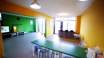 A brightly colored room with a green table and black stools, a television, and a fan.