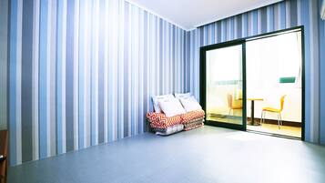 A modern room with a large sliding glass door leading to a balcony, striped wallpaper, and a bed with patterned bedding.