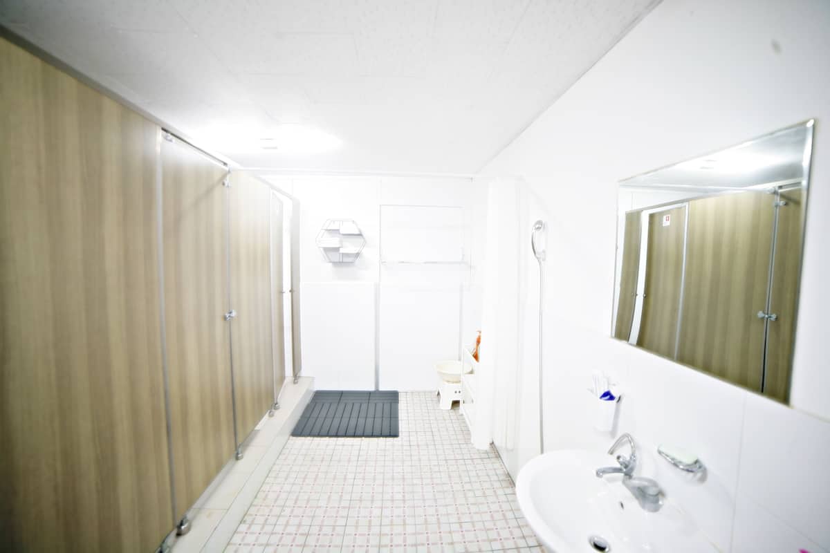 A small, brightly lit bathroom with a white sink, a mirror, and a shower stall.