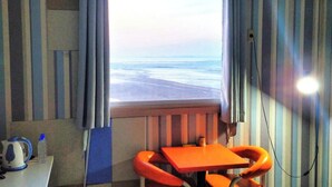 Una habitación con ventana que da a la playa, una mesa con hervidor y cortinas a rayas.