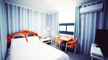 Een hotelkamer met een bed, een bureau, twee stoelen, een televisie en een raam.