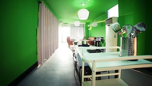 Una habitación con paredes verdes, una mesa larga, sillas y un escritorio con una computadora y varios objetos.