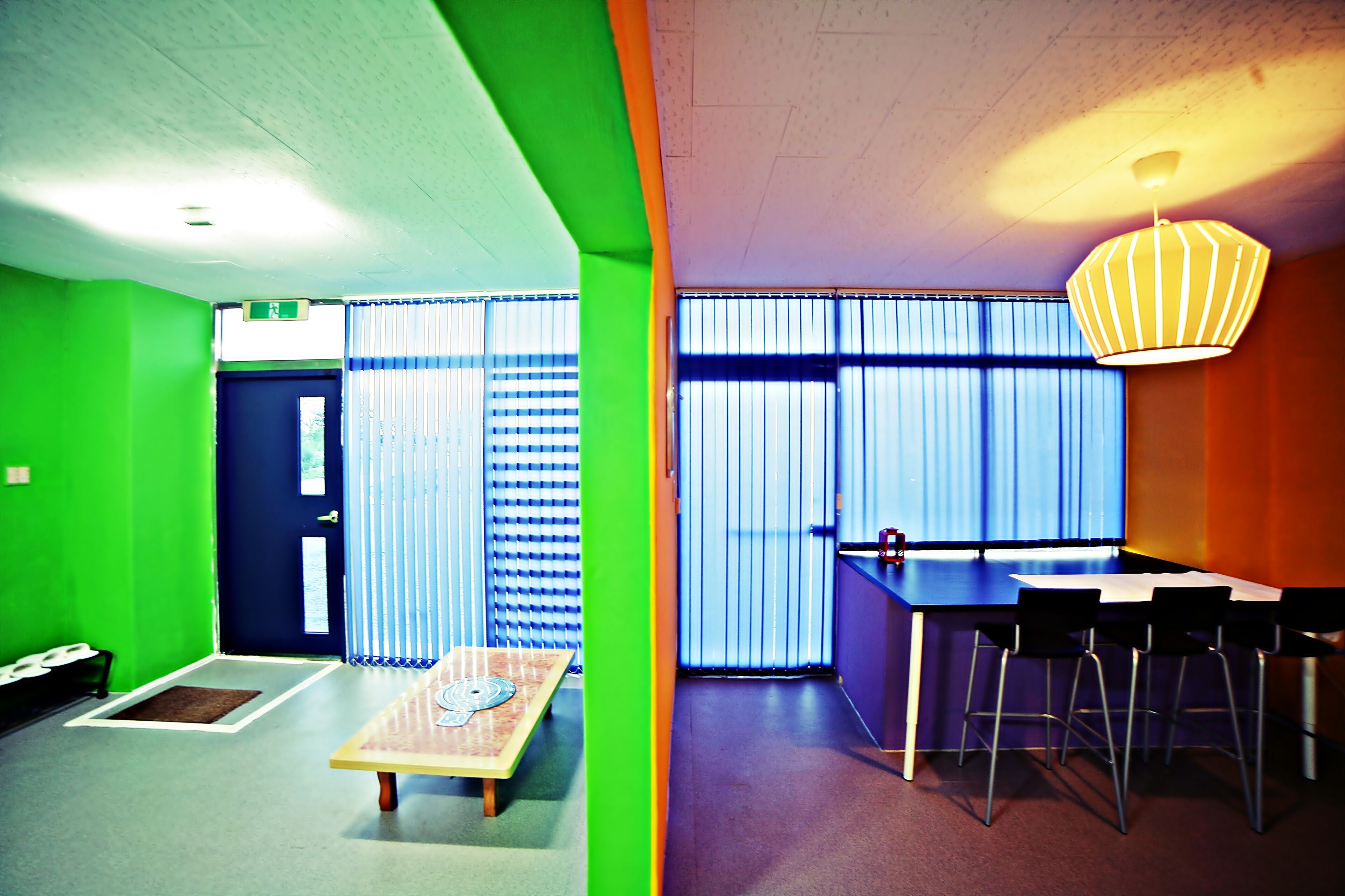 Une pièce avec un mur vert, une table en bois et un coin bar avec des tabourets.