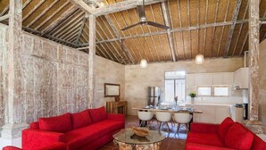 Een ruime woonkamer met rode banken, een glazen salontafel en een eethoek met witte stoelen.