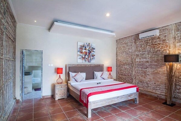 Un dormitorio con cama, lámparas de noche, aire acondicionado instalado en la pared y una puerta que da a un baño.