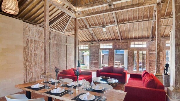 Een restaurant met een rustiek houten plafond, rode banken en een eettafel gedekt voor zes personen.