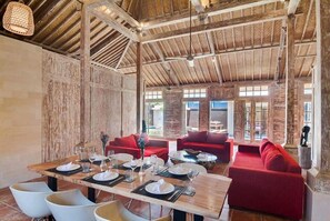 A restaurant with a rustic wooden ceiling, red sofas, and a dining table set for six. - Joglo Villa (Seminyak)