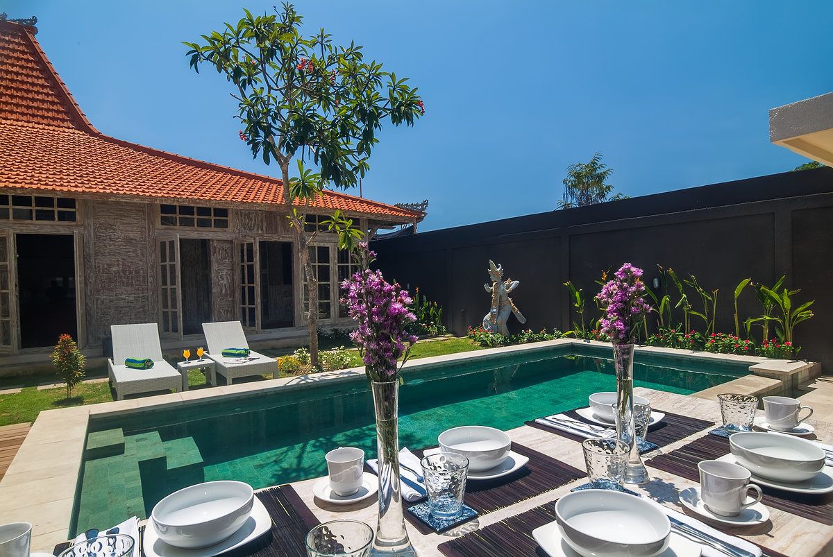 A poolside dining area with tables set for a meal, a pool, and a building with a tiled roof.