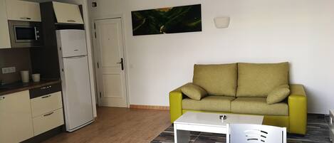 A compact living space with a kitchenette, a sofa, a dining table, and a potted plant.
