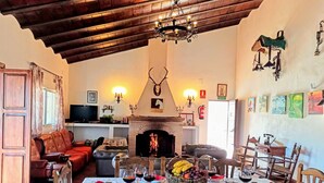 A cozy living room with a fireplace, a dining area with wooden chairs and a table set for a meal, and a television in the background.