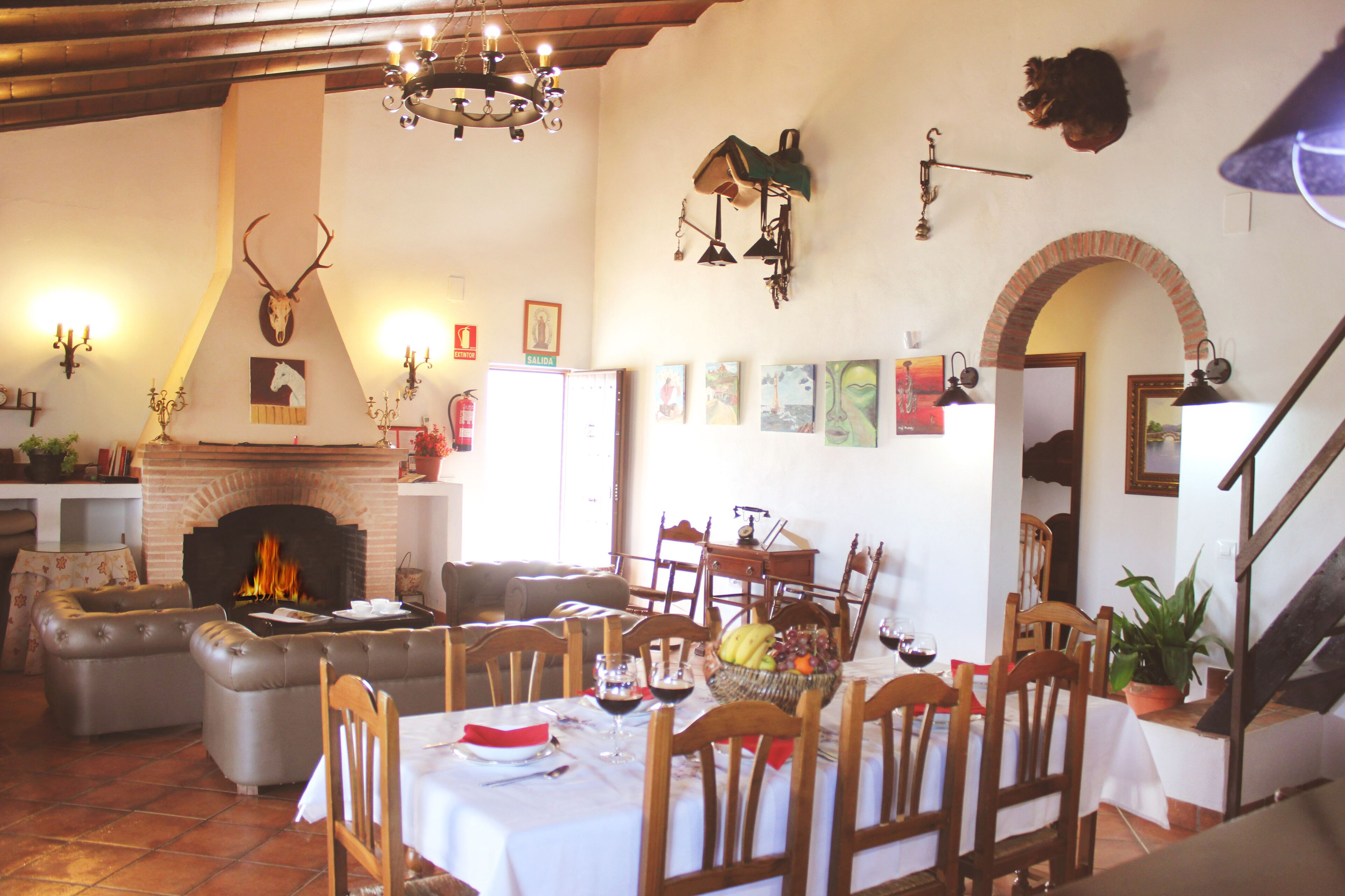 A dining area with a fireplace, wooden chairs, a table set for a meal, and a staircase leading to an upper level.