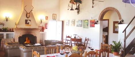 A dining area with a fireplace, wooden chairs, a table set for a meal, and a staircase leading to an upper level.