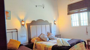 A room with two beds, a nightstand, a wall-mounted light fixture, and a window with blinds.
