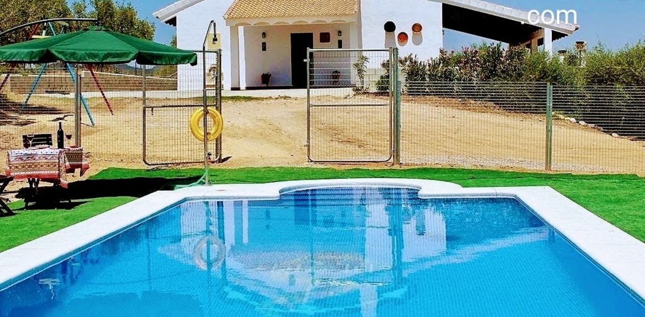 A rural villa with a swimming pool, a fenced area, and a small building.