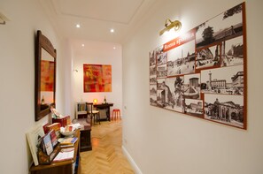 Um corredor com piso de madeira, uma escrivaninha com livros, uma cadeira e uma parede com pôster de 'Roma sparta'.