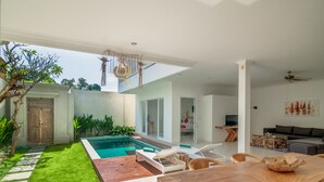 Un espacio exterior moderno con piscina, terraza de madera y sillones de descanso.