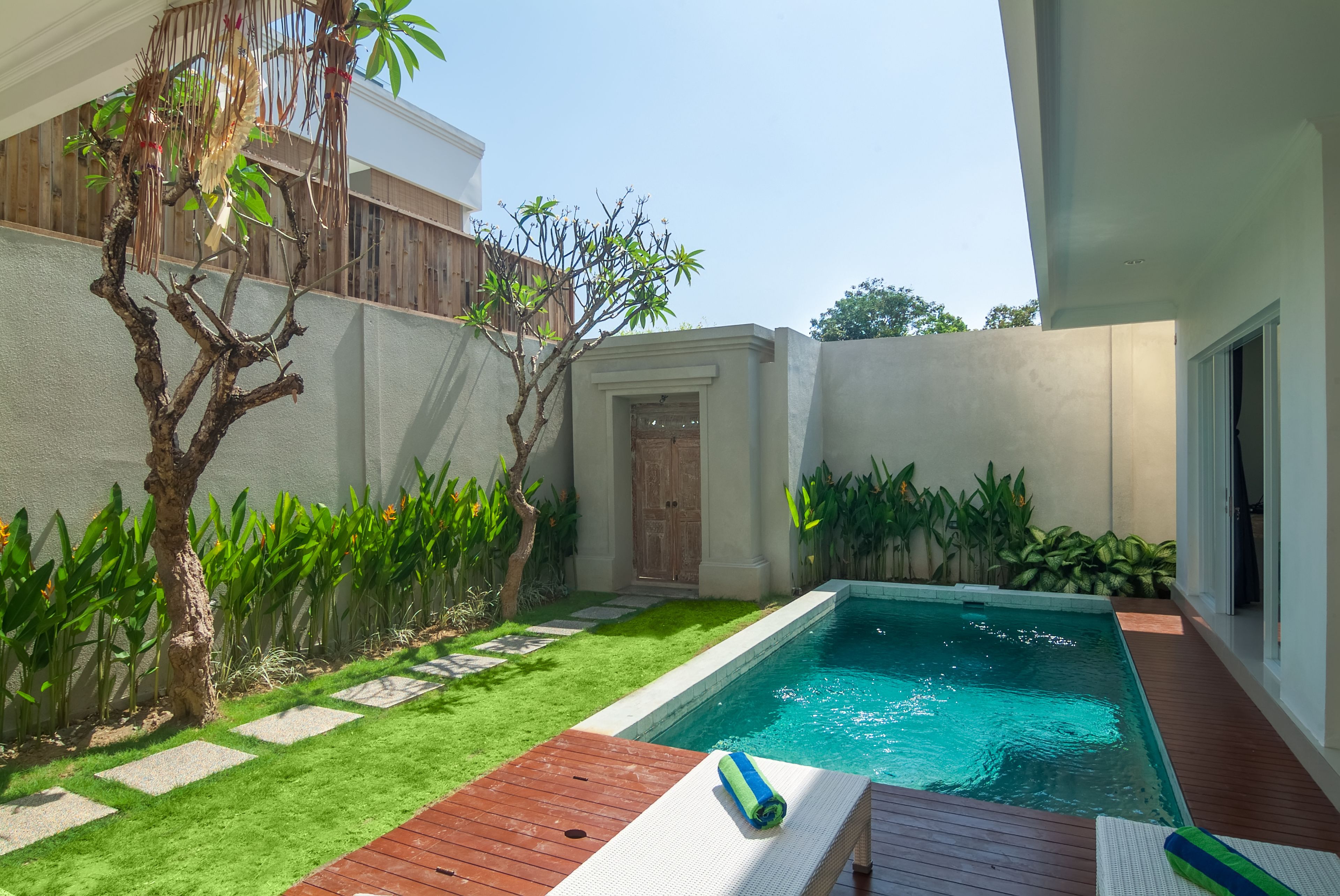 Una piscina con cubierta de madera, rodeada de césped cuidado y diversas plantas.