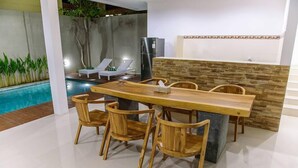 Un comedor moderno con una mesa y sillas de madera, una pared de acento de piedra y una piscina al fondo.