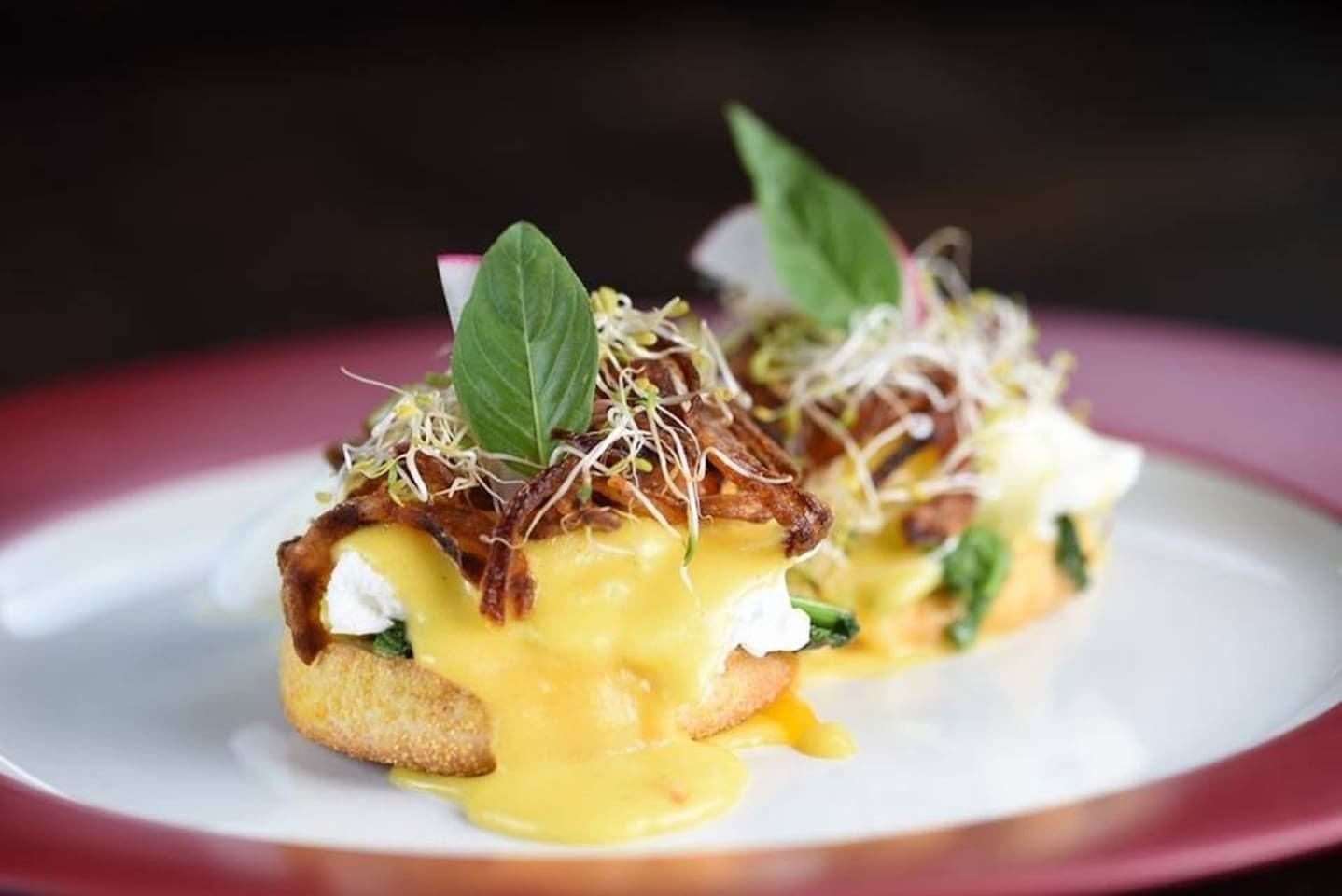 A plate with a dish consisting of a breaded item topped with a yellow sauce, greens, and a leaf garnish.
