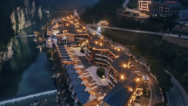 A riverside hotel with multiple buildings, a central courtyard, and a view of the river. - Spring Posh Roadsun International Hotel & Resort (Zhangjiajie)