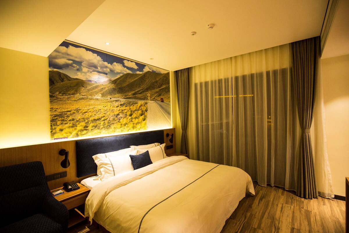 Ein Hotelzimmer mit einem großen Bett, einem Schreibtisch mit Stuhl, einem Nachttisch und einer Wandlampe.