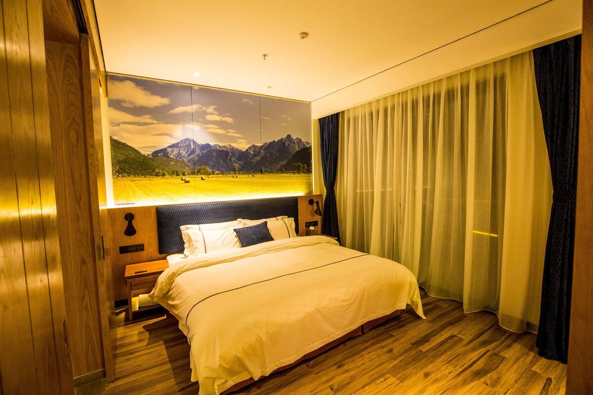 Ein Hotelzimmer mit einem großen Bett, Holzboden, Blick auf Berge durch ein Fenster und einem Nachthimmel.