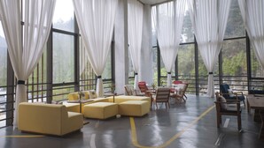 A spacious room with large windows, yellow sofas, wooden chairs, and a dining table. - Spring Posh Roadsun International Hotel & Resort (Zhangjiajie)