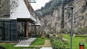 A modern building with a glass facade, outdoor seating area with chairs, and a well-maintained garden with a pathway leading to a wooden swing set. - Spring Posh Roadsun International Hotel & Resort (Zhangjiajie)