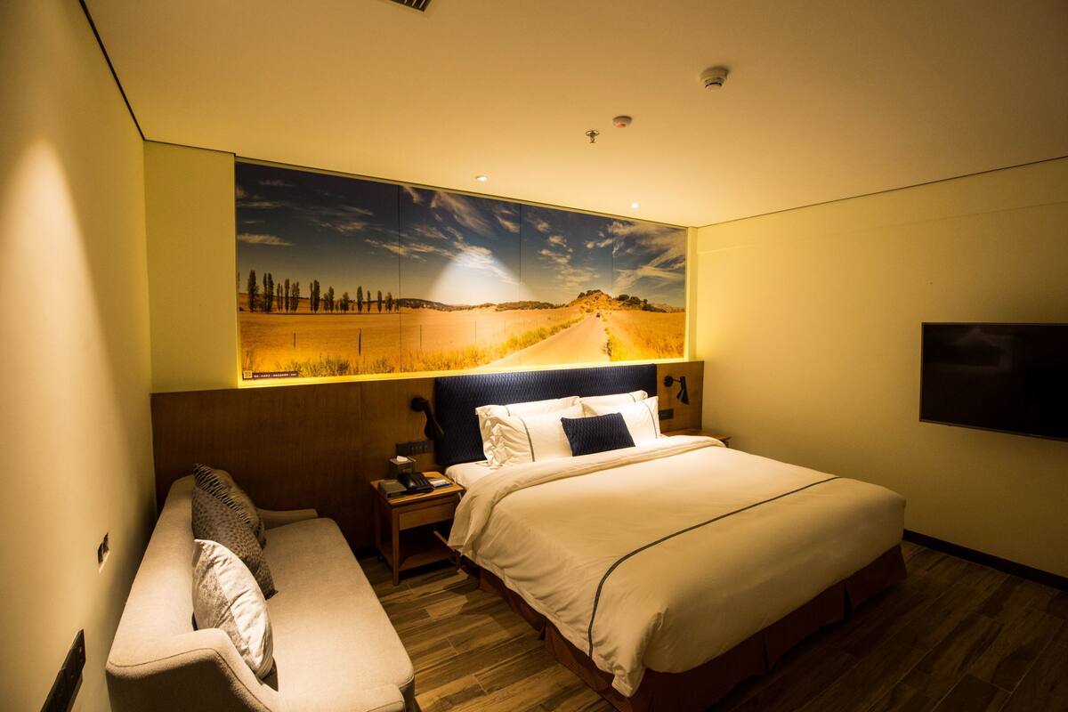 Ein Hotelzimmer mit einem großen Bett, einem Nachttisch, einer Schlafcouch und einem an der Wand befestigten Fernseher.