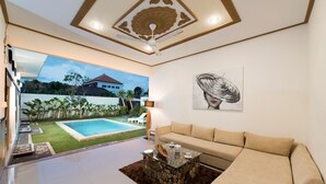 Uma sala de estar moderna com um sofá bege, uma mesa de centro de pedra e vista para uma piscina e jardim.