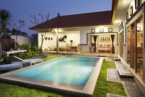 Une piscine avec un espace patio, un coin salon abrité et une pelouse bien entretenue.
