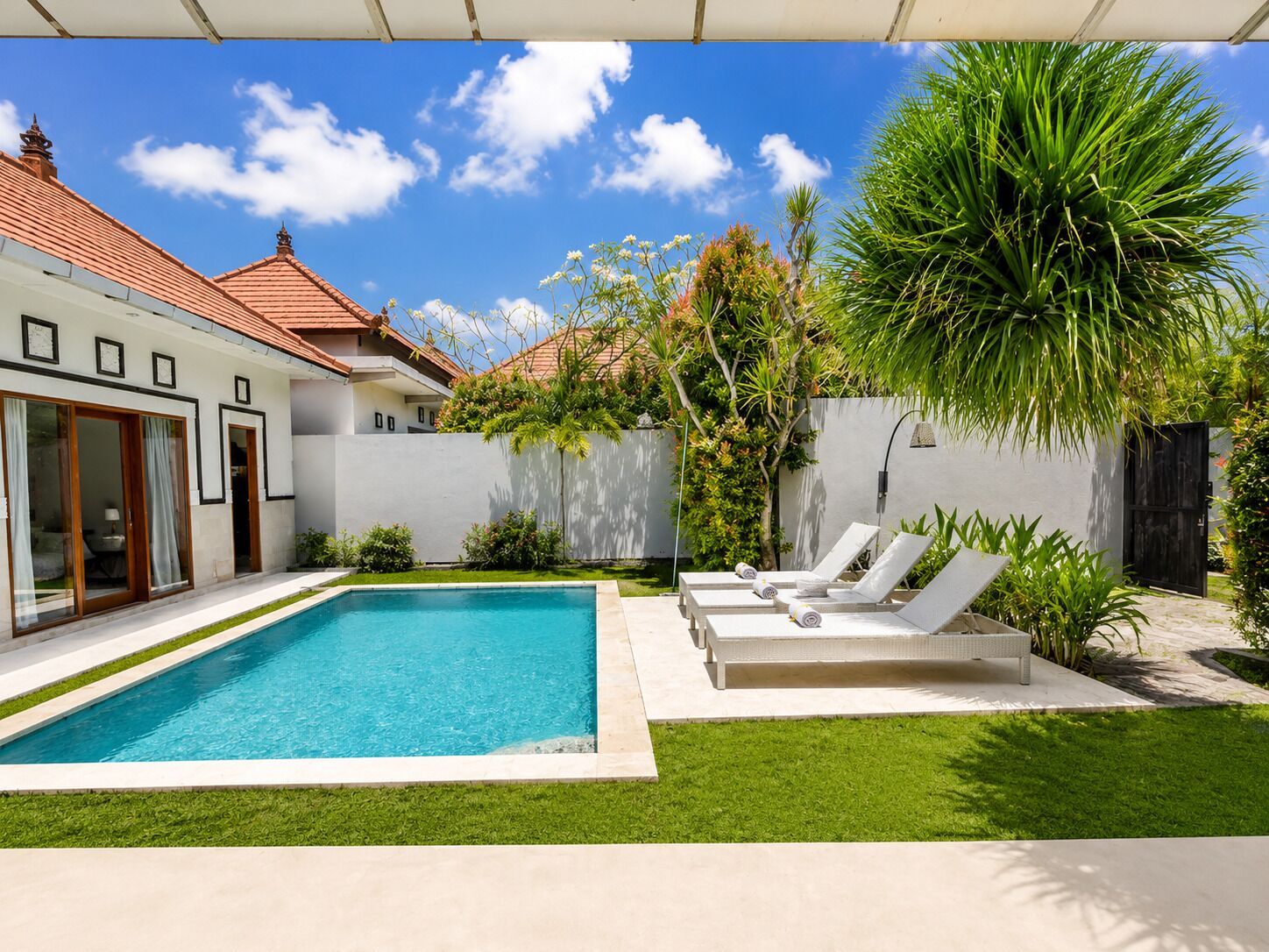 A modern pool area with a clear blue pool, surrounded by a well-maintained lawn and a variety of tropical plants.