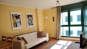 A living room with a sofa, a coffee table, a TV, and a large window with curtains. - Barreiros Apartment - Catedrales Beach 5 pers. (2 rooms) views to the Foz Estuary (Barreiros)