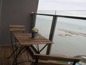 A balcony with a wooden table and bench, a potted plant, and a view of a river and distant landscape. - Vinz at Silverscape Luxury Residence (Malacca City)
