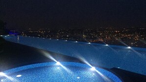 Vista nocturna de una piscina con luces de ciudad al fondo.