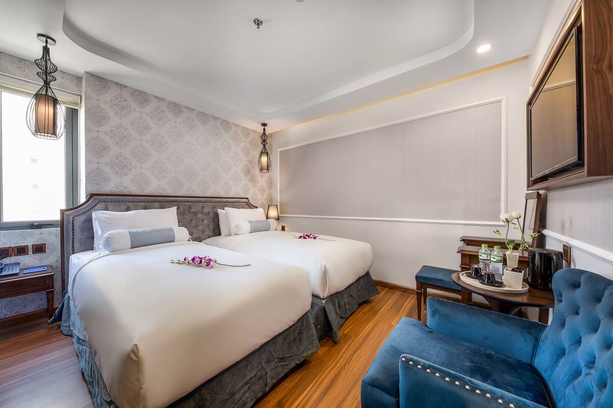 A hotel room with two beds, a blue armchair, a small table with a tray, and a large mirror.