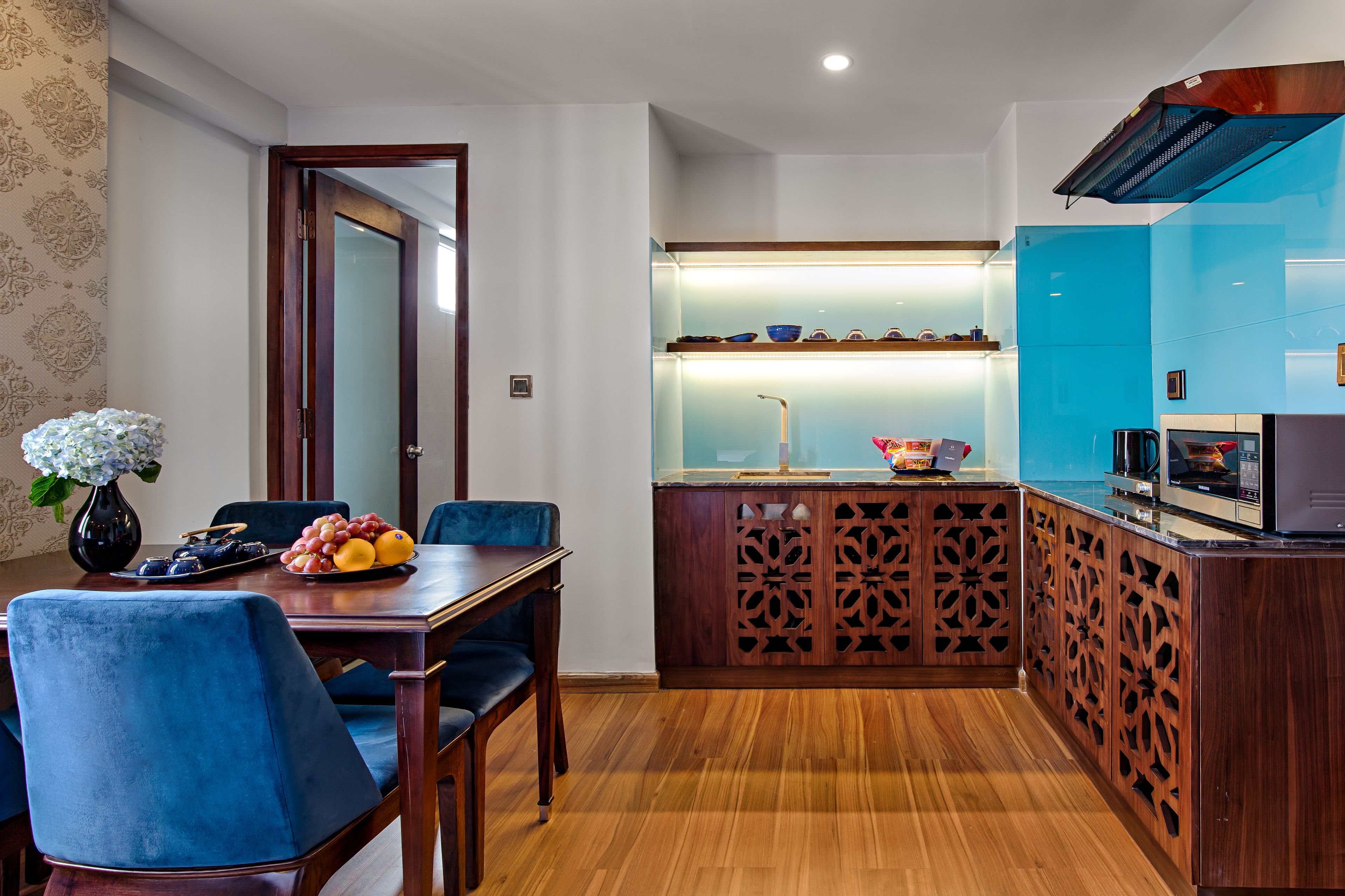 A modern kitchen with a wooden dining table, blue chairs, and a fruit bowl.