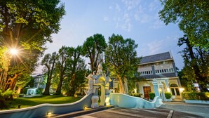A grand entrance with a curved pathway leading to a building, surrounded by lush greenery and trees. - At Pingnakorn Riverside Hotel Chiangmai (Chiang Mai)