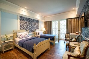 A hotel room with two beds, a sitting area with chairs, a TV, and a patterned wall. - At Pingnakorn Riverside Hotel Chiangmai (Chiang Mai)