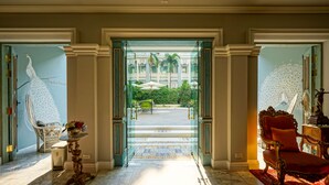 A grand entrance with a glass door leading to a courtyard, a white chair with a vase of flowers, and a red chair with a red rug. - At Pingnakorn Riverside Hotel Chiangmai (Chiang Mai)