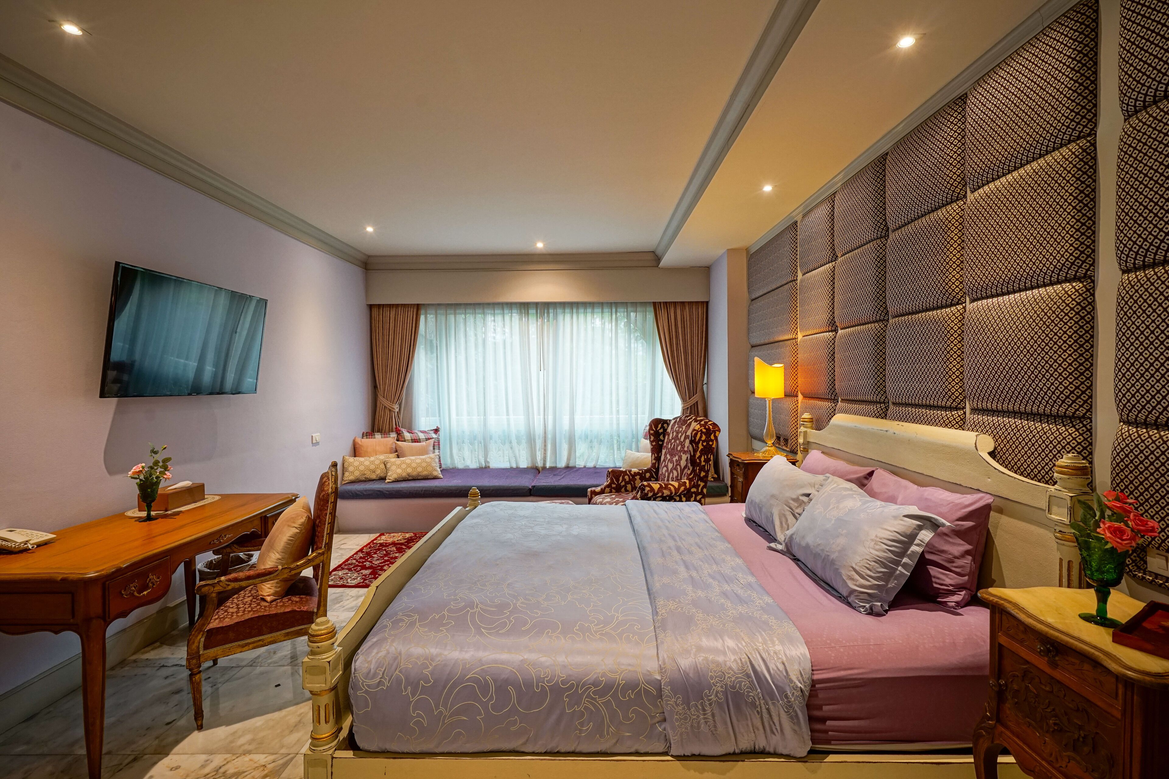 A hotel room with a large bed, a desk, a chair, a sofa, and a TV.