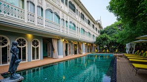 A swimming pool with a tiled deck, a statue, and a building with ornate windows and balconies. - At Pingnakorn Riverside Hotel Chiangmai (Chiang Mai)