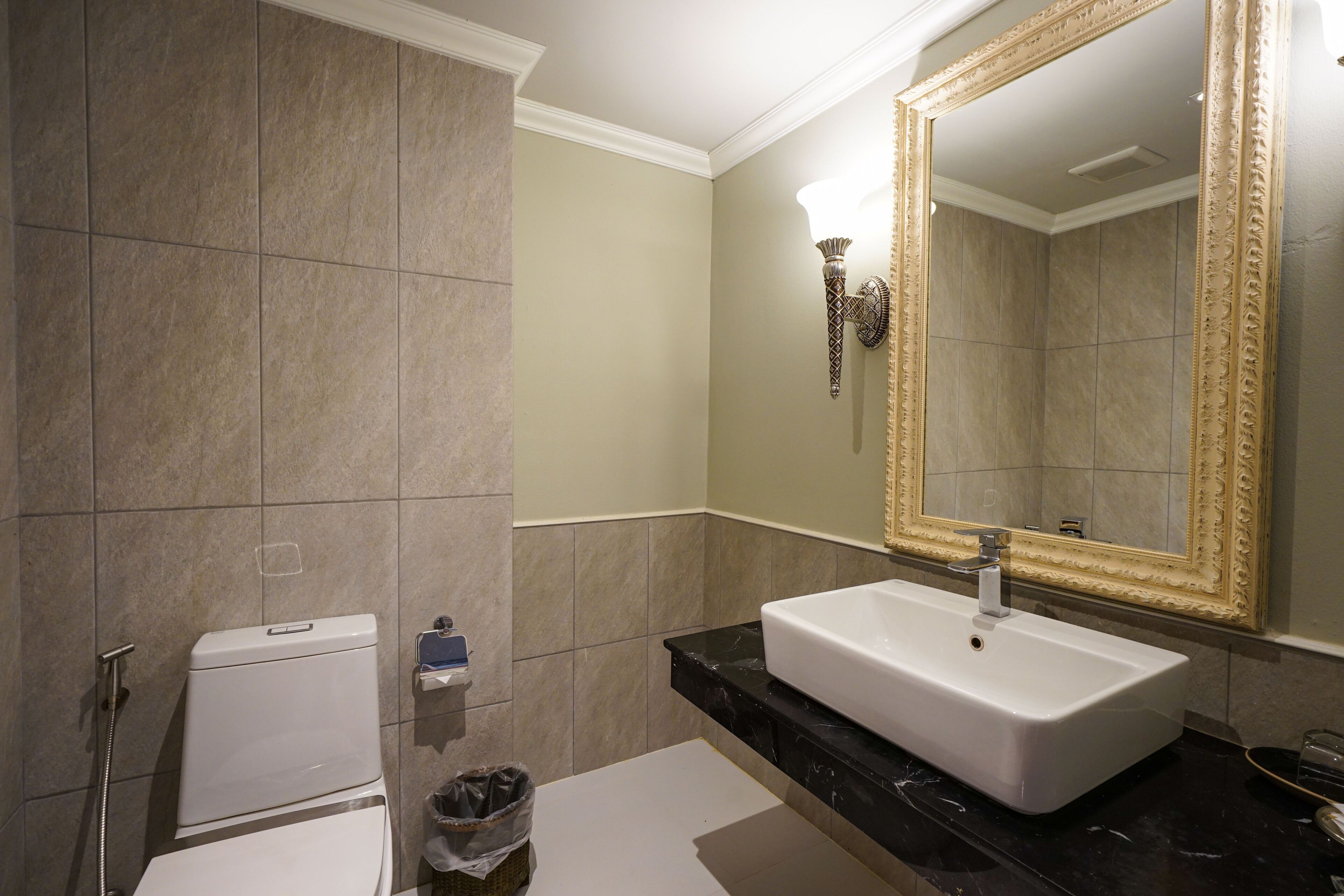 Um banheiro com pia branca, um espelho grande com moldura decorativa e vaso sanitário.
