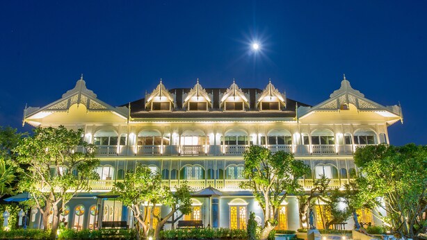 A large, ornate building with multiple balconies and a prominent central tower, surrounded by lush greenery. - At Pingnakorn Riverside Hotel Chiangmai (Chiang Mai)